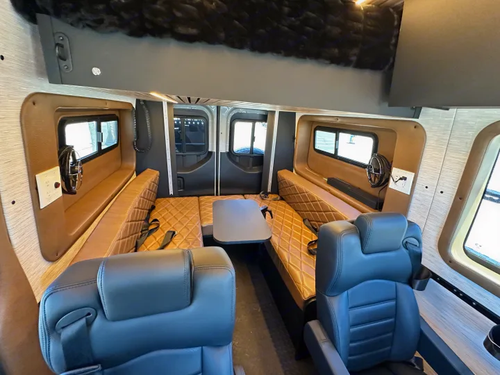 Spacious RV rental interior with convertible tan benches, overhead bunk, captain's chairs, and power outlets.. Rogue Van Rogue Van Class B 2025