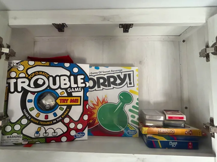 RV rental game storage: Classic board games Trouble, Sorry!, Skip-Bo, and Phase 10 organized in a white cabinet.. Heartland RVs Trail Runner 2024