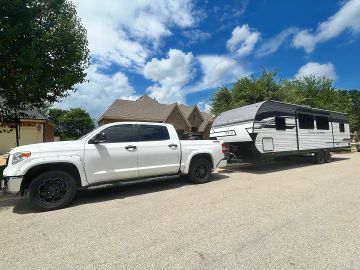 A white Toyota Tundra pickup towing a gray & white "TRAIL RUNNER" travel trailer RV. Ideal for your next rv rental trip.. Heartland RVs Trail Runner 2024