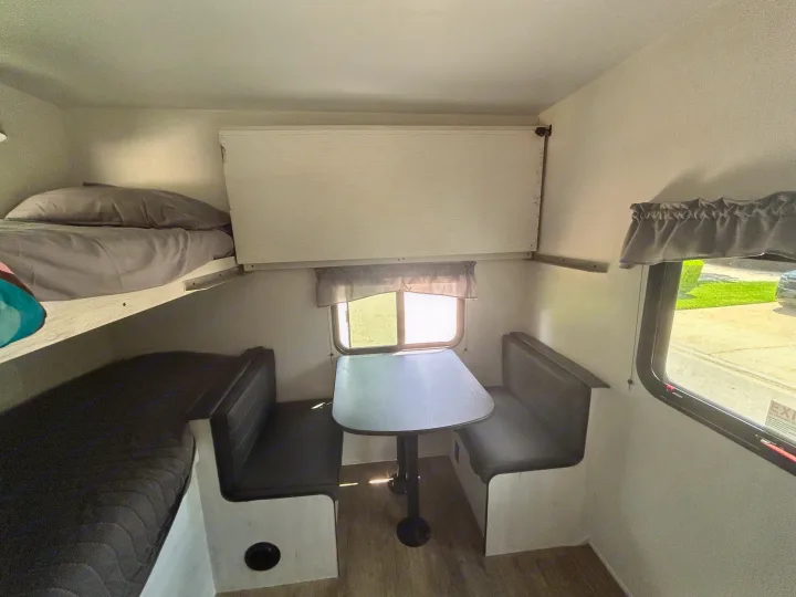 RV rental interior: a bright dinette with a table and benches, a cozy bunk bed, and a window overlooking the outdoors.. Heartland RVs Trail Runner 2024