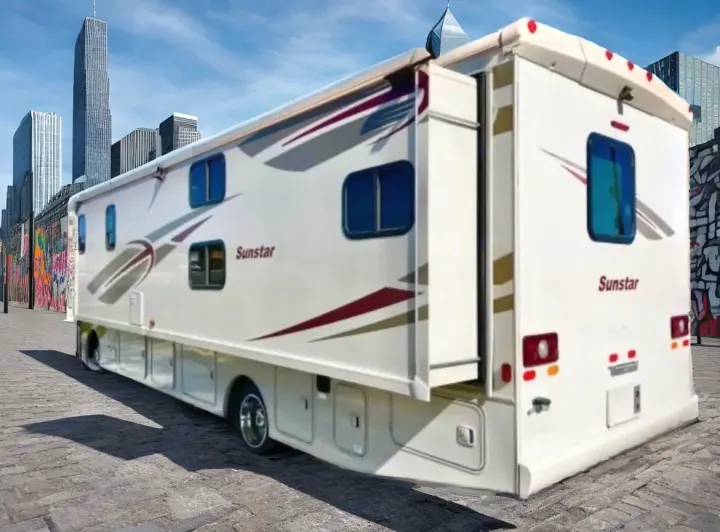 This white Sunstar RV rental, with an extended slide-out, is parked on a city street near skyscrapers and a graffiti wall, ready for adventure.. Winnebago Sunstar 2016