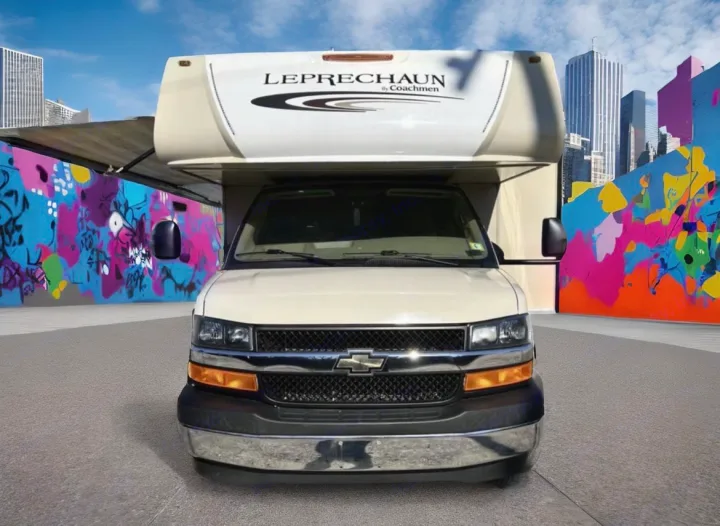 White Chevrolet Leprechaun RV rental parked head-on against colorful graffiti walls and a city skyline.. Coachmen Leprechaun 2018