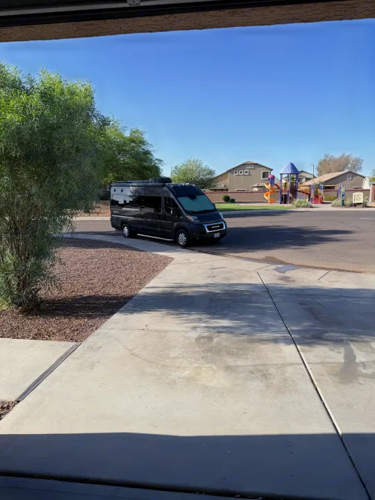 Black camper van **rv rental** parked on a residential street, with a colorful playground in the background under a clear blue sky.. Jayco Swift Li 2023