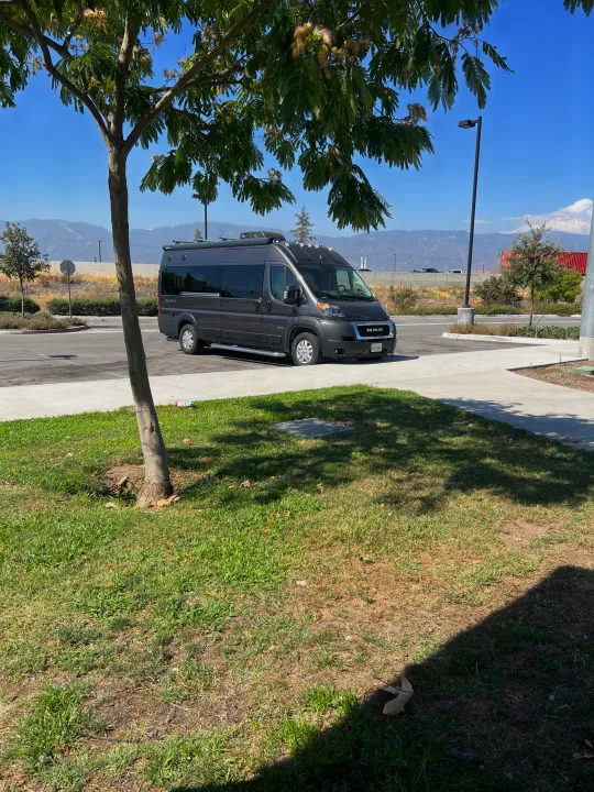 A dark grey Jayco RAM ProMaster RV rental is parked in a sunny lot, with mountains and trees in the background.. Jayco Swift Li 2023