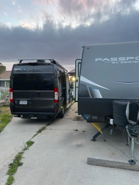 An rv rental setup: dark camper van and Passport travel trailer parked on a driveway under an overcast sky.. Jayco Swift Li 2023