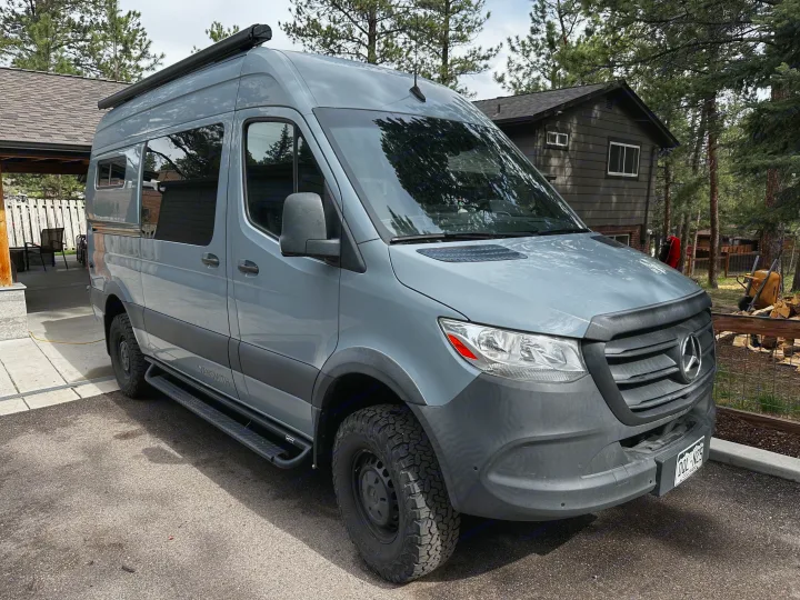 Gray Mercedes Sprinter adventure van, a perfect rv rental, parked near a cabin. Explore van life travel & outdoor experiences.. Mercedes-Benz Sprinter 2020