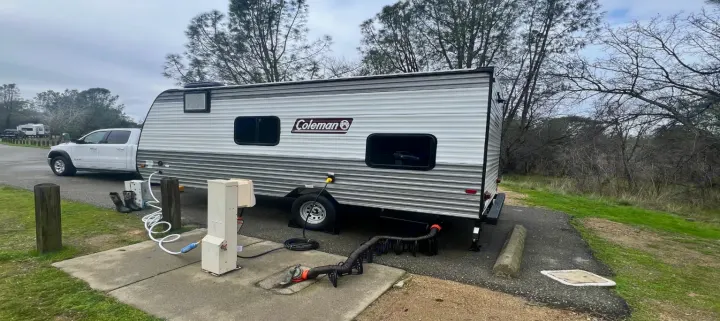 This rv rental, a Coleman travel trailer, is hooked up at a cloudy campsite with a white Ram truck and full utilities.. Dutchmen Coleman Lantern LT 2024