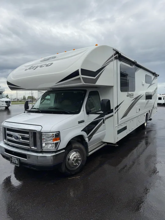 White Jayco Redhawk Class C RV rental parked on wet pavement under a cloudy sky. Montana license plate visible.. Jayco Redhawk 2020