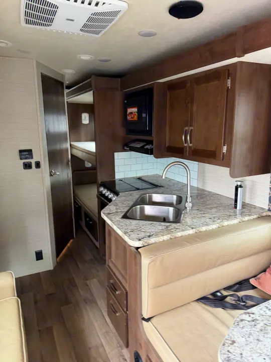 RV rental interior featuring a kitchen with double sink, stovetop, microwave, dinette seating, and bunk beds.. Jayco Redhawk 2020