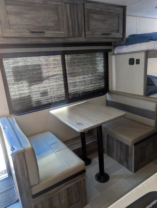 Modern RV rental dinette with grey benches, wood cabinets, and a peek of bunk beds, offering a comfy interior space.. Forest River Wildwood FSX Plantium 2022