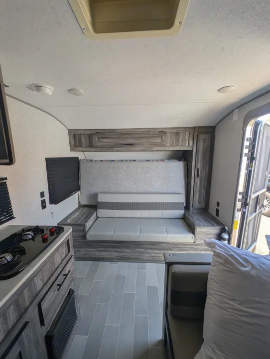 Inside a modern rv rental: compact kitchen with stovetop, gray woodgrain cabinets, and a dinette that converts to a bed.. Forest River Wildwood FSX Plantium 2022