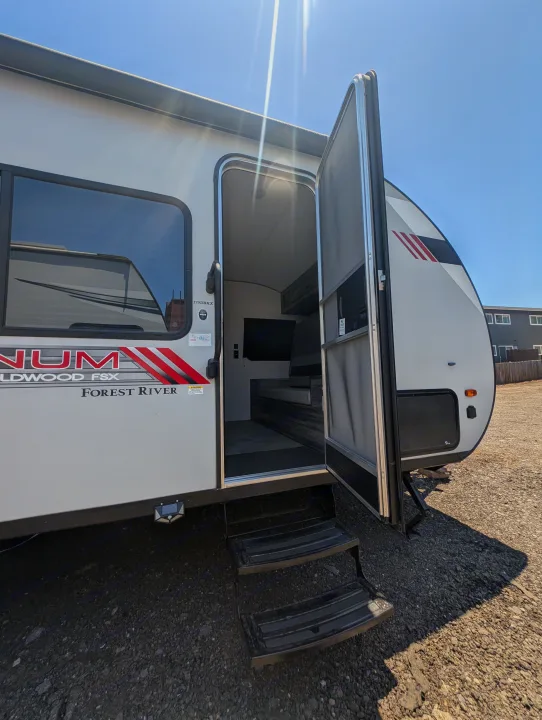Open door of a white Forest River Wildwood FSX travel trailer, showing its interior and steps, ideal for an rv rental.. Forest River Wildwood FSX Plantium 2022