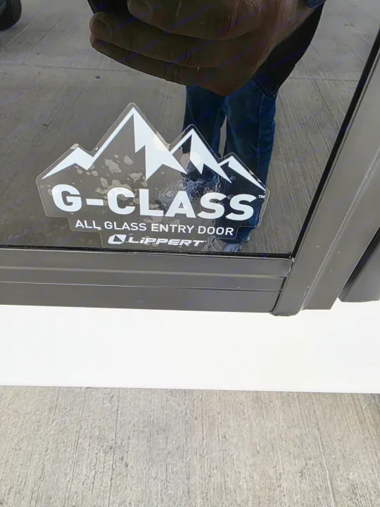 G-Class All Glass Entry Door by Lippert on an rv rental. Mountain logo and reflections of the ground and a person.. Crossroads RV Sunset Trail Super Lite 2025