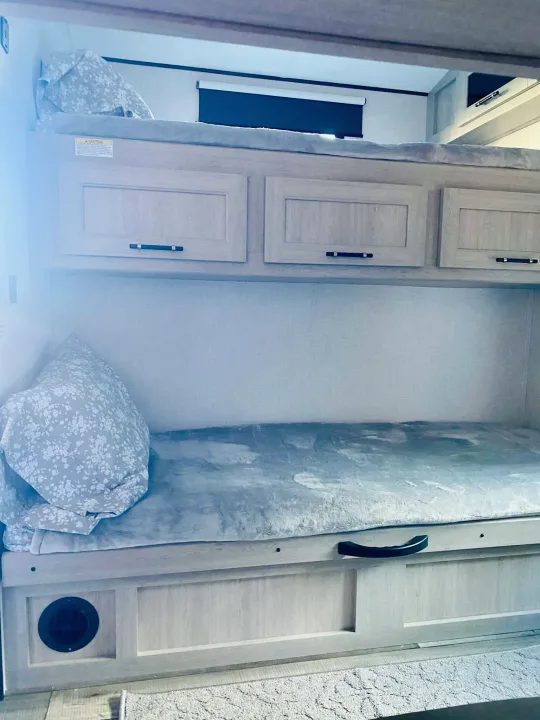 RV rental bunk beds feature two sleeping areas, overhead cabinets, and a lower drawer for storage. Light wood interior with cozy bedding.. Crossroads RV Sunset Trail Super Lite 2025