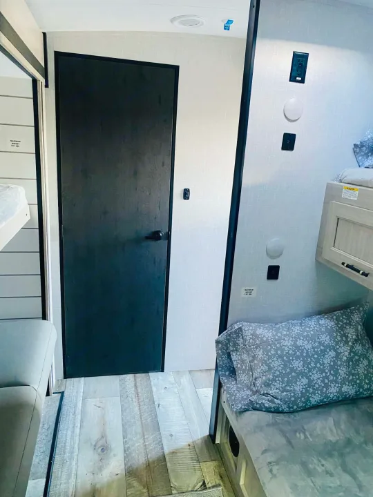 RV rental interior featuring bunk beds, a dark door, wood-look flooring, and functional wall outlets for a compact living space.. Crossroads RV Sunset Trail Super Lite 2025