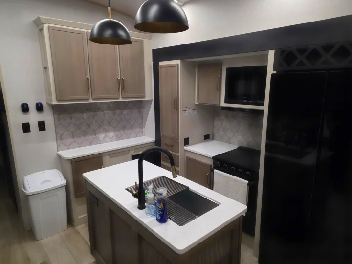 Modern RV rental kitchen featuring a central island, black appliances, light cabinets, and a stylish backsplash.. Forest River Salem Hemisphere 2025