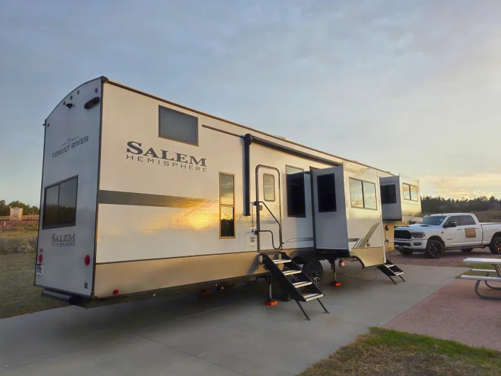This spacious Forest River Salem Hemisphere RV rental, with slides extended, is parked at a campsite beside a white Ram truck.. Forest River Salem Hemisphere 2025