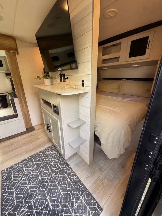 Cozy RV rental interior with a bright bedroom, wall-mounted TV, and modern wood-look floor.. Heartland RVs North Trail 2022