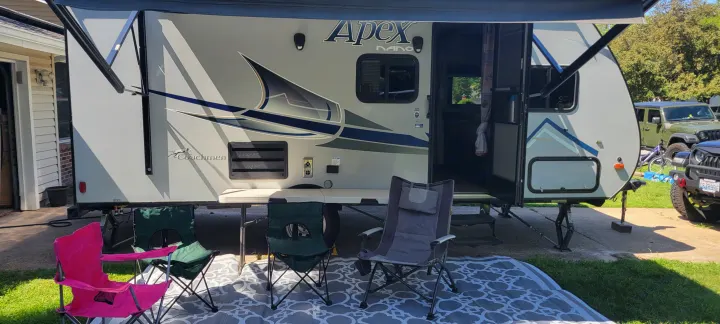 RV rental with an open door, extended awning, and an outdoor setup with camping chairs on a patterned rug.. Coachmen Apex Nano 2017
