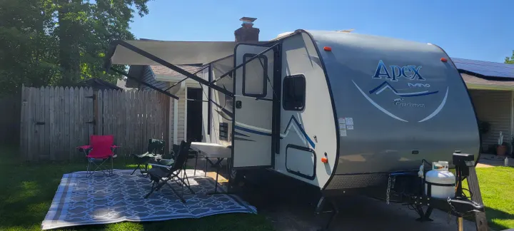 An Apex Nano rv rental, with an extended awning, outdoor rug, and chairs, set up for backyard leisure on a sunny day.. Coachmen Apex Nano 2017