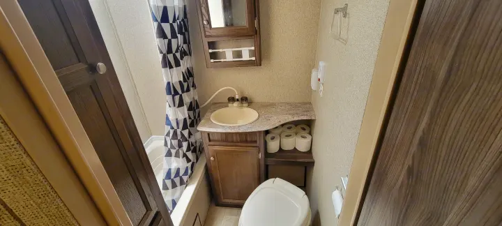 This compact RV rental bathroom features a shower/tub, vanity, toilet, and convenient toilet paper storage, ideal for travel.. Coachmen Apex Nano 2017