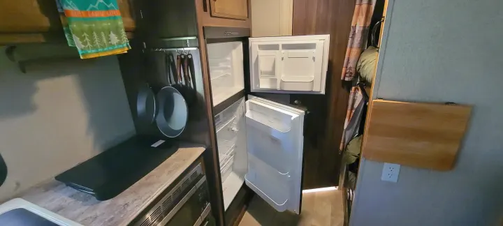 Inside an RV rental: kitchen area featuring an open fridge, microwave/oven, hanging pans, and a space-saving foldable table.. Coachmen Apex Nano 2017