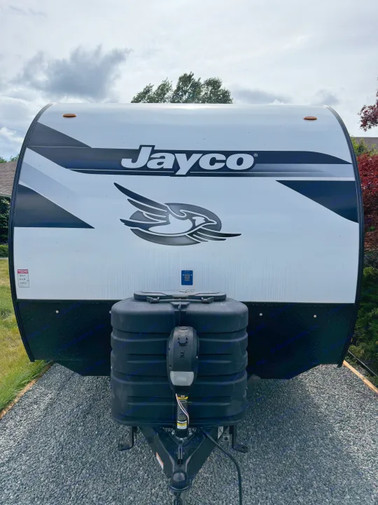 Front view of a white Jayco travel trailer RV, featuring propane tanks on gravel, under a cloudy sky. Consider this rv rental!. Jayco Jay Feather Micro 2025
