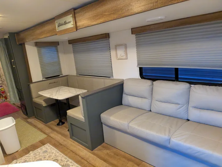 Cozy RV rental interior: L-shaped dinette with marble-look table and comfortable light grey sofa, framed by wood accents.. Eddie Bauer Eddie Bauer 2024