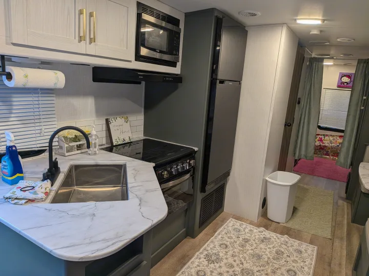 A clean, modern rv rental kitchen featuring a microwave, stove, fridge, sink, white countertops, and dark gray cabinetry.. Eddie Bauer Eddie Bauer 2024