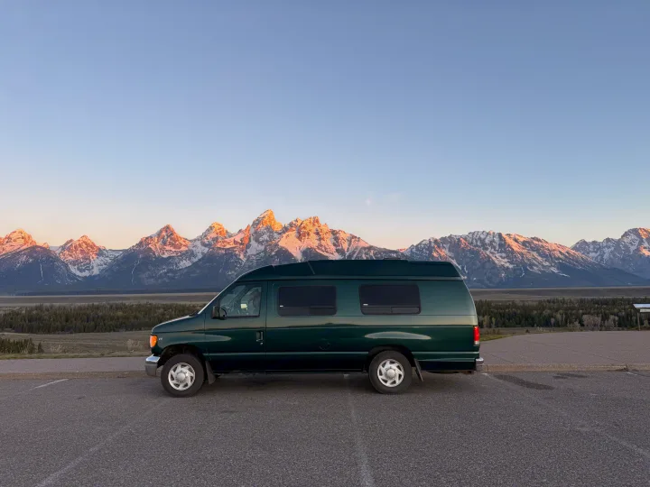Dark green RV rental van overlooking majestic, sun-kissed snow-capped mountains and forest at sunrise/sunset. A scenic vista.. Ford Econolline 250s 2001
