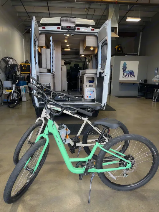Two bikes in front of a white camper van with its rear doors open, showing the interior. Ideal for an rv rental adventure!. Winnebago Solis 59PX 2023