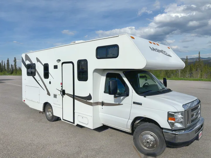 This white Majestic rv rental, a Class C motorhome, is parked in a scenic spot with trees and mountains under a blue sky.. Thor Majestic 2020