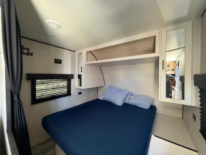 RV rental bedroom interior: blue bed, overhead storage, window, and mirrored cabinet for comfortable travel.. Jayco Jay Flight SLX 2025