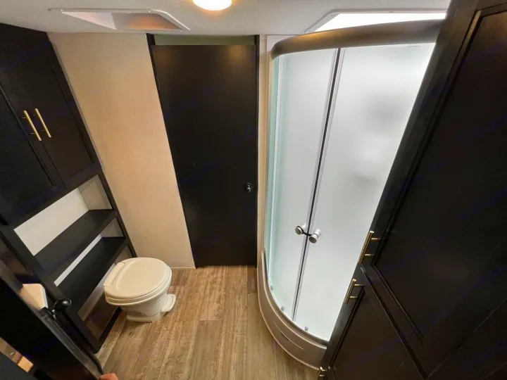 RV rental bathroom features a compact toilet, curved glass shower, and dark cabinetry with shelving. Modern, functional design.. Forest River Cherokee Grey Wolf 2022