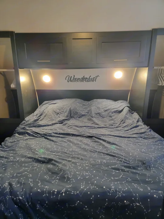 Cozy RV rental bedroom featuring a constellation-patterned bed, overhead storage, and a "Wanderlust" sign.. Forest River Cherokee Grey Wolf 2022