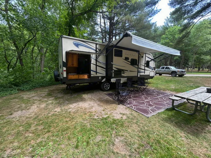 RV rental travel trailer at a shaded campsite. Awning, outdoor kitchen, chairs, and picnic table ready for outdoor living.. Crossroads RV Sunset Trail Reserve 2014