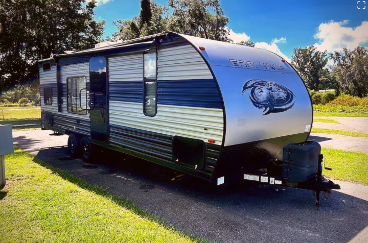 This stylish Grey Wolf travel trailer RV rental, featuring blue stripes, is parked under a bright sky, ready for your next adventure.. Forest River Cherokee Grey Wolf 2022