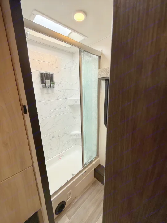 RV rental shower interior with white tiled walls, glass door, dispenser, and ceiling light. Bright and clean.. Forest River Sunseeker MBS 2022