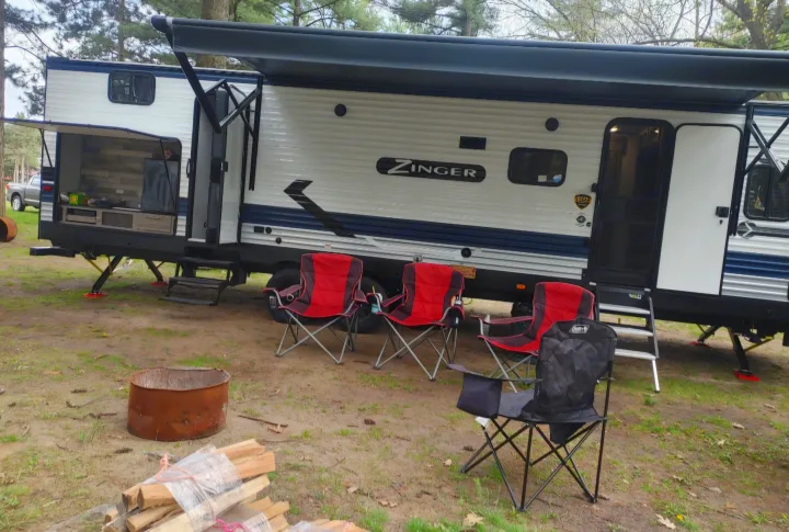 RV rental: A Zinger travel trailer with an extended awning, outdoor kitchen, camping chairs, and a fire pit in a scenic campground.. Crossroads RV Zinger 2021