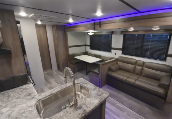 RV rental interior: Kitchen with sink, comfortable dinette booth, and sofa with blue accent lighting. Ready for travel.. Crossroads RV Zinger 2021