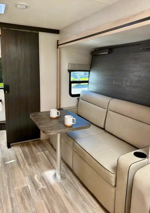 Modern RV rental interior: a comfy dinette sofa with two mugs on the table, sleek flooring, and a convertible bed setup.. Forest River Sunseeker MBS 2022