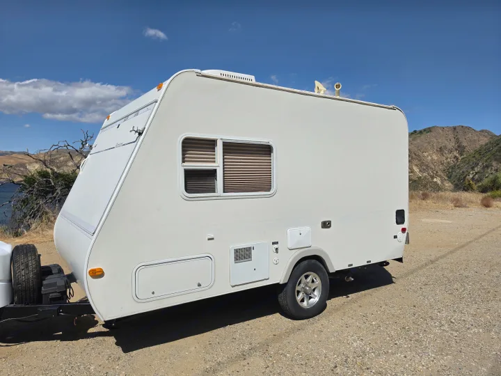 White travel trailer for RV rental parked on a scenic dirt road. Mountains, blue sky, and a lake create a beautiful outdoor adventure setting.. R-Vision Trail-Lite Bantam 2002