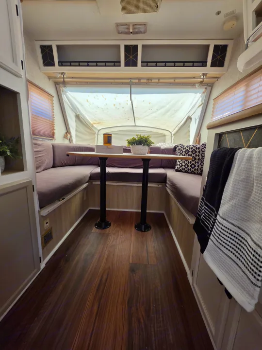 Cozy RV rental interior featuring a U-shaped dinette, table, wood floors, and a bright pop-up camper end.. R-Vision Trail-Lite Bantam 2002