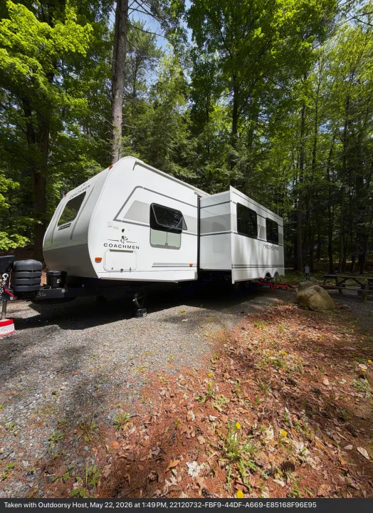 White travel trailer rv rental set up at a shaded forest campsite with extended slide-out and picnic table.. Coachmen 29 SE 2025