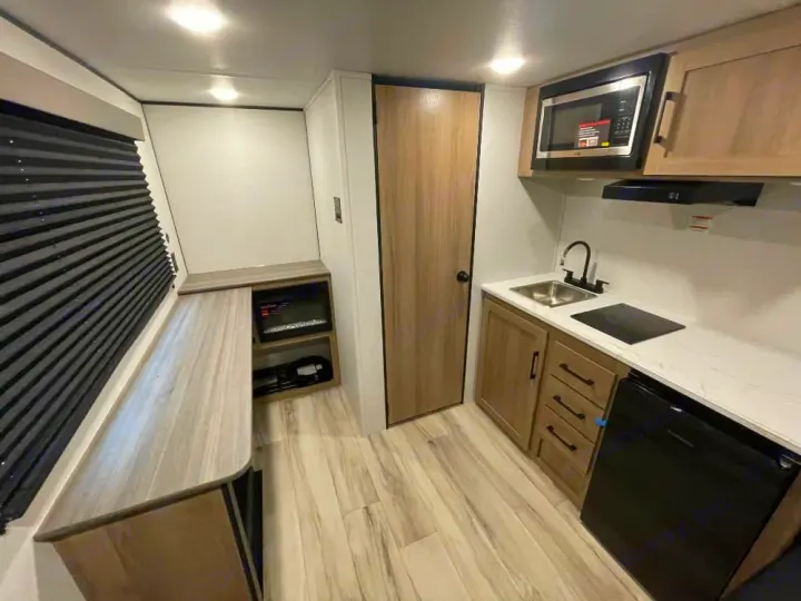 Bright RV rental interior features a compact kitchen with microwave, sink, fridge, and a long bench with storage.. Keystone RV Coleman 2026