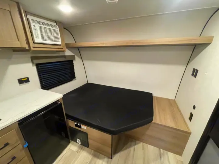 Cozy RV rental interior with a comfortable bed, AC unit, window, and kitchenette featuring an under-counter fridge.. Keystone RV Coleman 2026