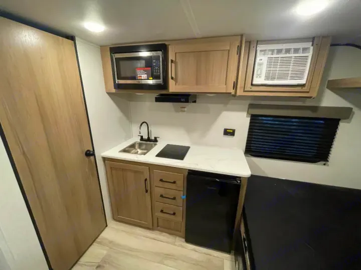This modern, compact kitchen in an RV rental features a microwave, sink, stove, fridge, and wall-mounted AC unit.. Keystone RV Coleman 2026