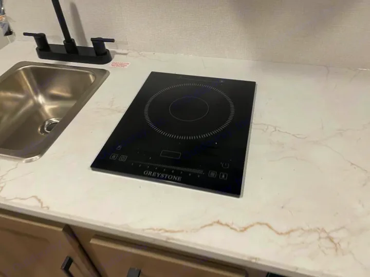 Compact RV rental kitchen featuring a modern induction cooktop, sink, and faucet on a patterned countertop.. Keystone RV Coleman 2026