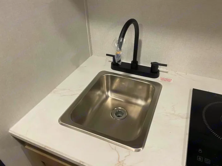 Modern RV rental kitchen featuring a stainless steel sink, black gooseneck faucet, and induction cooktop on a light marbled counter.. Keystone RV Coleman 2026
