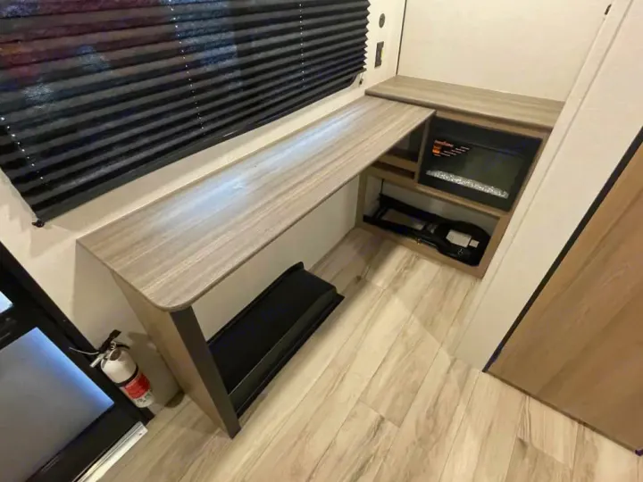 RV rental interior: modern desk, electric fireplace, wood-look floor, and a visible fire extinguisher by the entry door.. Keystone RV Coleman 2026